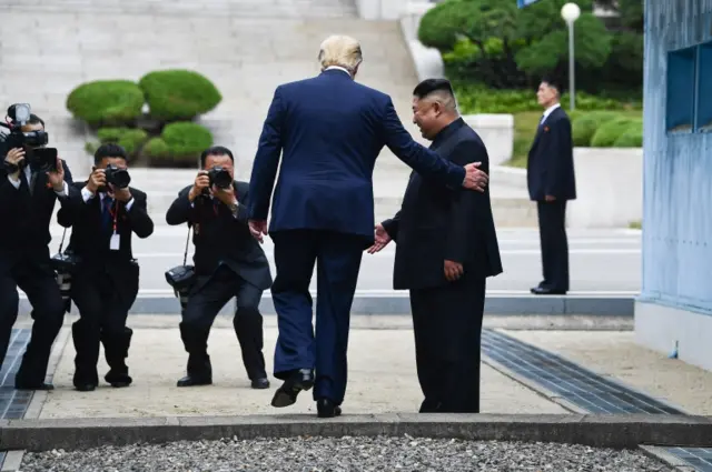 US President Donald Trump steps into the northern side of the Military Demarcation Line that divides North and South Korea, as North Korea"s leader Kim Jong Un looks on, in the Joint Security Area (JSA) of Panmunjom in the Demilitarized zone (DMZ) on June 30, 2019.