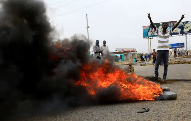 A man stands next to a barricade of tyres set alight