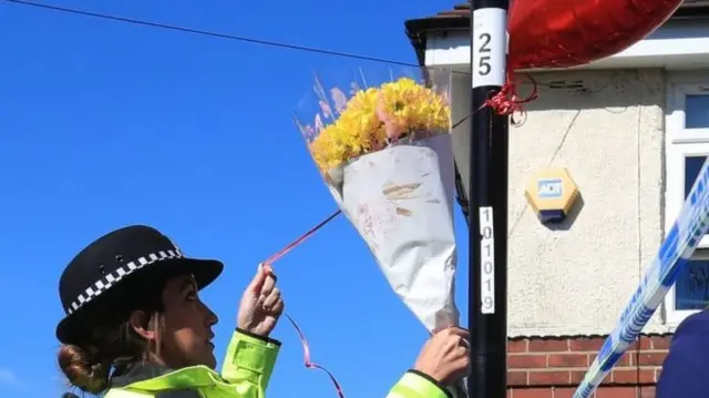 A police officer ties flowers to a lamppost