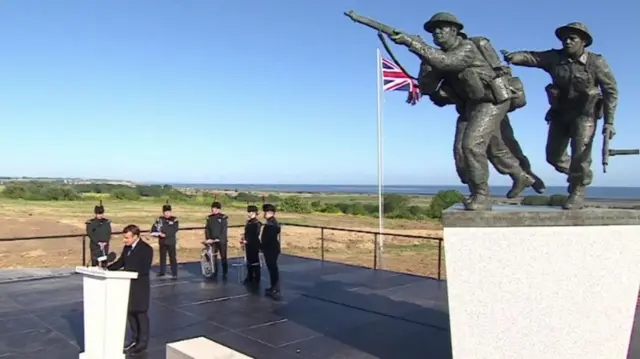Macron speaks besides the statue