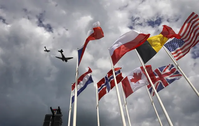 Planes and flags fly over the beach at Arromanches