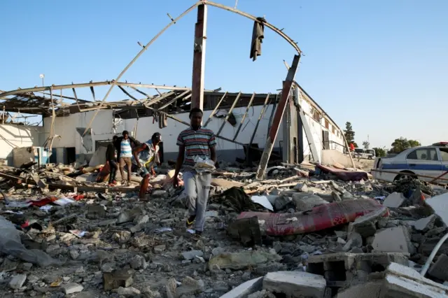 Migrants carry the remains of their belongings from among rubble at a detention centre for mainly African migrants that was hit by an airstrike in the Tajoura