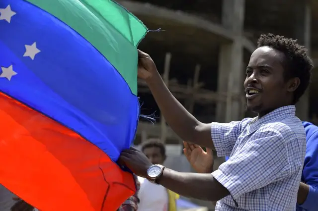 A man waving the unofficial flag in red, blue and turquoise of the Sidama ethnic group