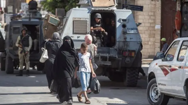 Woman walking down street with child past tanks