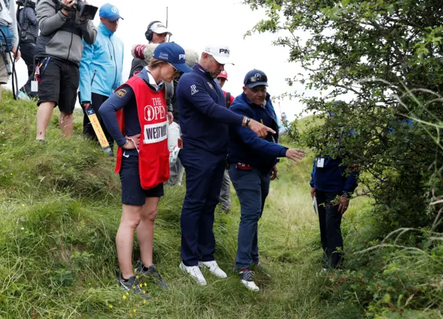 Lee Westwood discusses his options after his wayward shot into a bush on the 10th hole