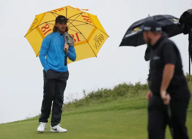 Tommy Fleetwood and Shane Lowry get out the umbrellas on the sixth hole