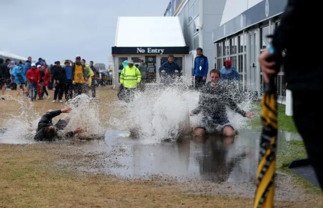 Fans slide through puddles at The Open