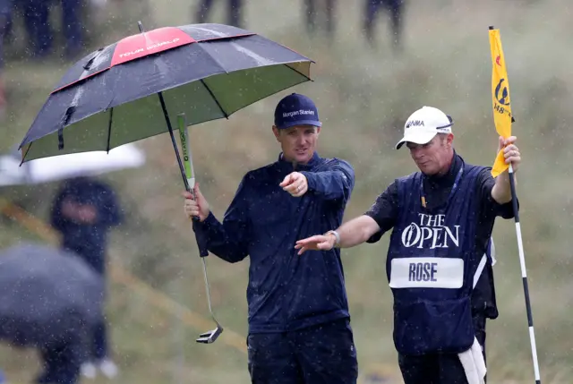 Justin Rose shelters under an umbrella with his caddie on the eighth hole