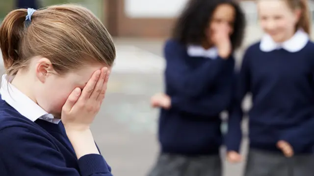 Schoolchildren whispering in playground about another child