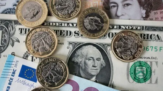 Pound coins atop dollar and euro notes