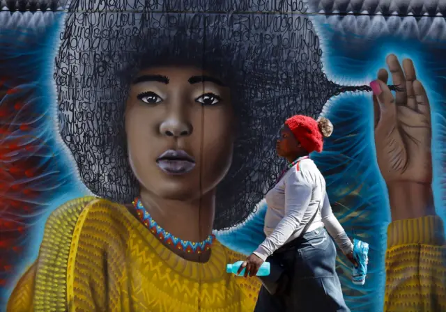 A woman walks past a graffiti artwork on the walls in the trendy Maboneng district of Johannesburg, South Africa, 30 July 2019.