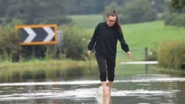 Woman walking in flooded road in Prestbury, Cheshire