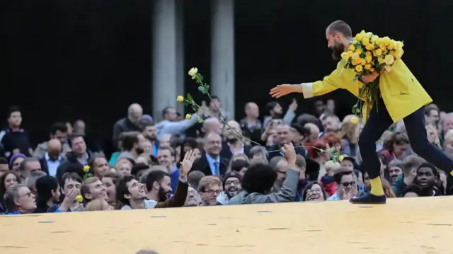 A man walking down a catwalk hands out roses to the audience