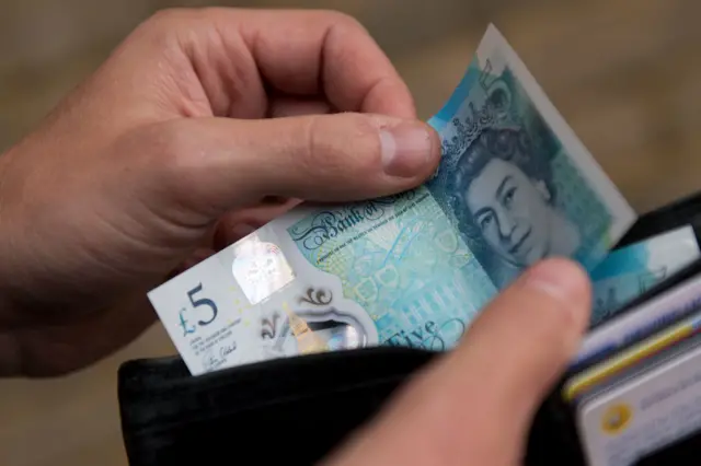 A hand taking a £5 note out of a wallet