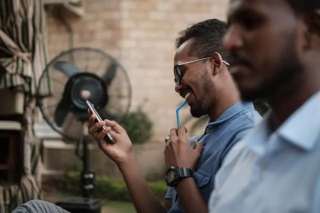 Sudanese men use their smart-phones to access the internet at a cafe