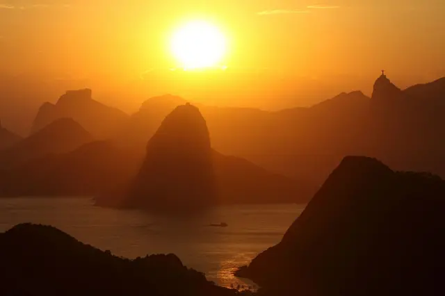 Overview of the mountains of Rio de Janeiro and entrance of Guanabara Bay at sunset with Sugar Loaf Mountain in the center, Pedra da Gavea ( Rock of Gavea ) at left - background and Corcovado Mountain with Christ the Redeemer Statue atop of it at right, Brazil.