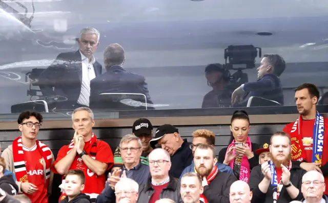 Jose Mourinho sits in the TV studio behind Manchester United fans watching the match