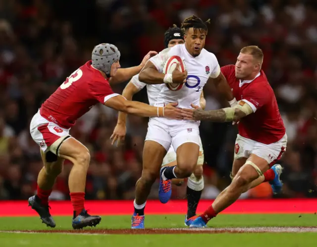 Anthony Watson of England breaks through the tackle of Jonathan Davies and Ross Moriarty of Wales