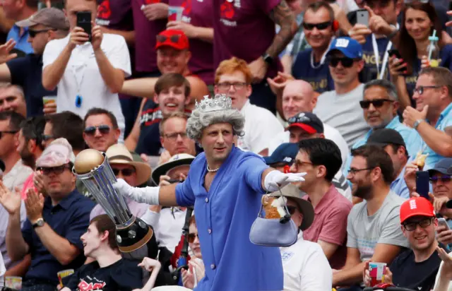 A fan in fancy dress holds a replica World Cup trophy