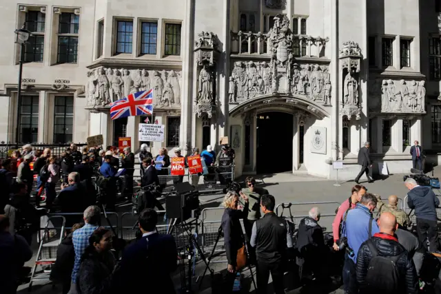 Protesters and media gather outside the court entrance in Westminster