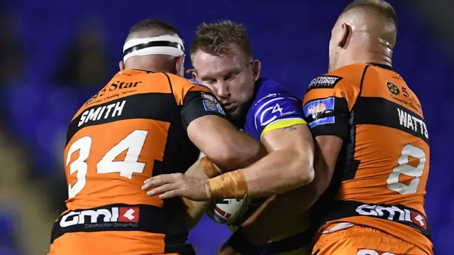 Mike Cooper of Warrington Wolves is tackled by Daniel Smith and Liam Watts of Castleford Tigers