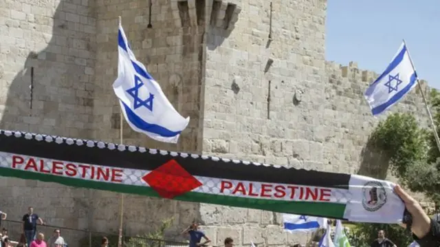 Palestine scarf in foreground with Israeli flags in the background