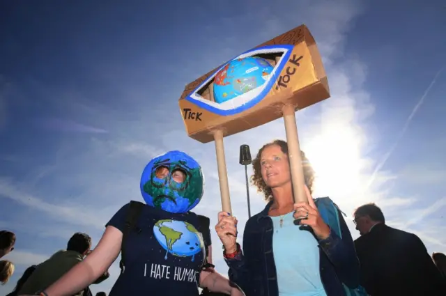 Two protesters in Cullercoats, one wearing a globe as a head and another holding a globe aloft with the words "tick tock" written on it