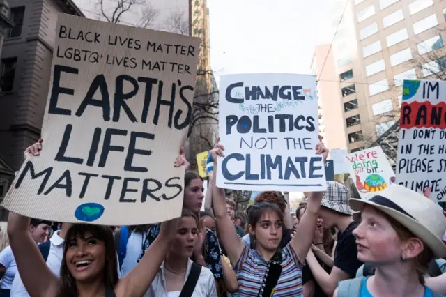 Protesters in Melbourne, Australia, holding signs saying "Change the politics not the climate" and "black lives matter, LGBTQ+ lives matter, Earth's life matters"