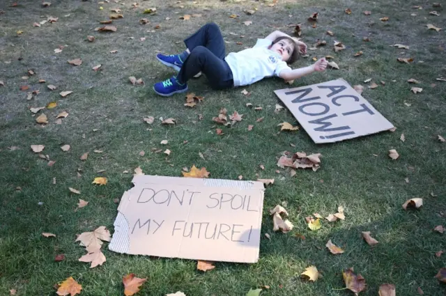 Child on the ground with signs reading "don't spoil my future" and "act now!"