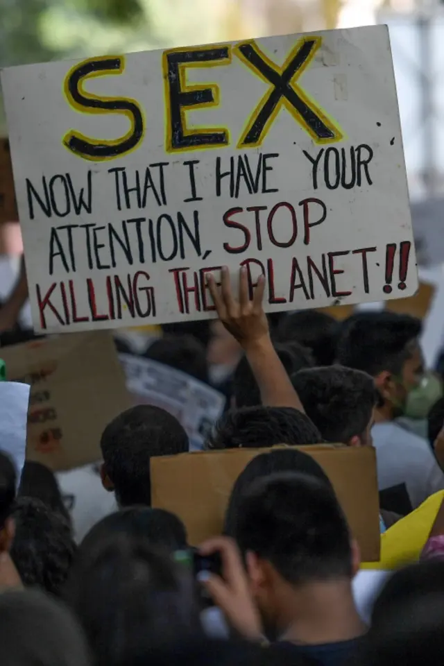 Protester in New Delhi holding a sign that says: "SEX. Now that I have your attention, stop killing the planet!"