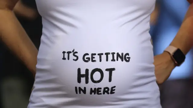 A pregnant woman's stomach - she is wearing a t-shirt which says: "It's getting hot in here"