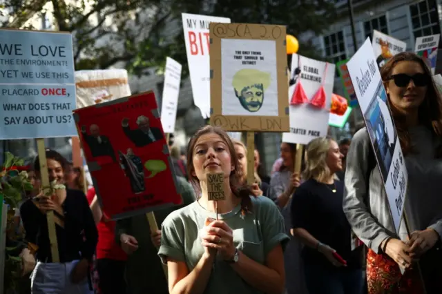 Protesters in London with signs reading "save the trees" and "We love the environment! Yet we use this placard once - what does that say about us?"