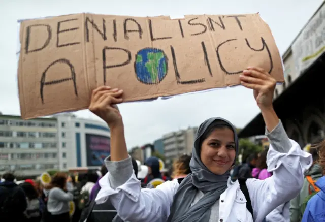 A woman in Istanbul holding a sign that says "Denial isn't a policy"