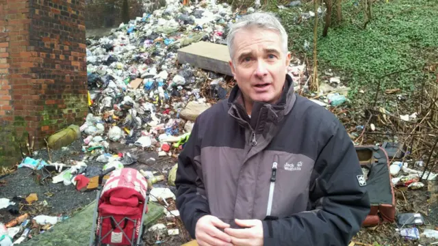 A reporter stands in front of fly tipping