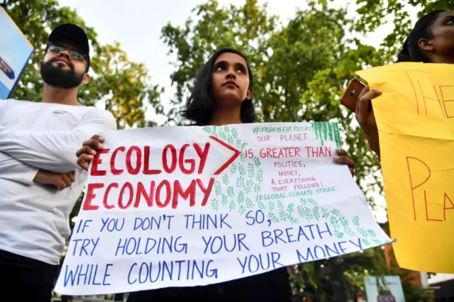 Protester in Guwahati with a sign that says "Ecology > economy - if you don't think so, try holding your breath while counting your money"