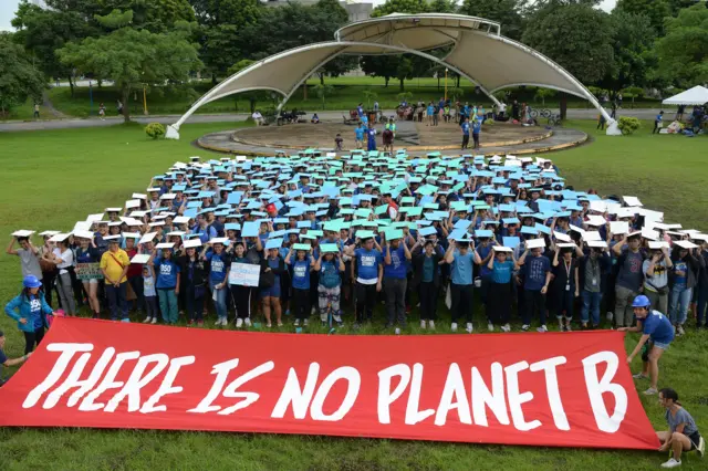 Dozens of students stand behind a large sign which reads "there is no planet B"