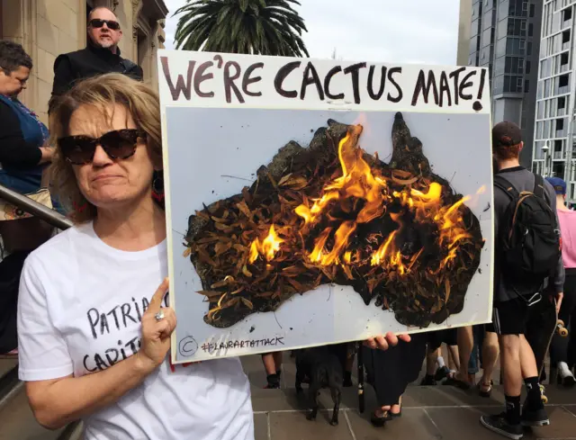 A protester in Melbourne holds a sign saying, "We're cactus, mate"