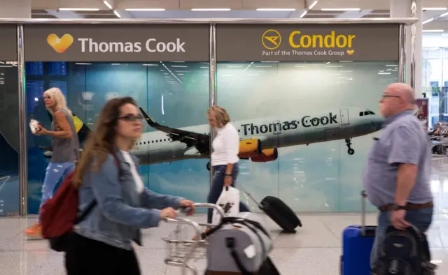 Passengers walk past Thomas Cook sign