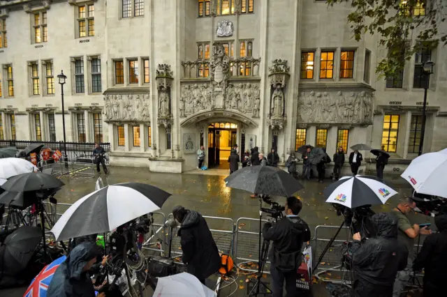 Media huddle under umbrellas as rain falls in London