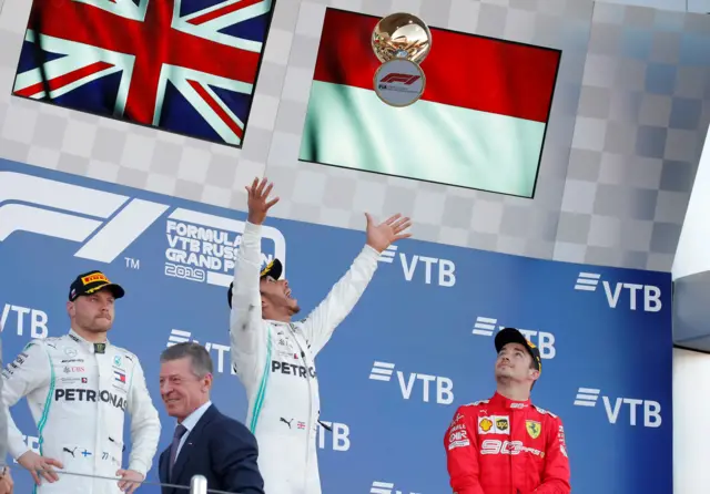 Lewis Hamilton throws the trophy in the air on the podium, with Charles Leclerc and Valtteri Bottas watching on