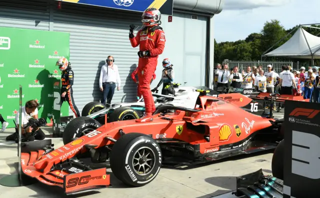 Charles Leclerc pumps his fist while standing on his Ferrari