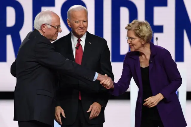 Joe Biden, centre, looks on as senators Bernie Sanders, left, and Elizabeth Warren shake hands