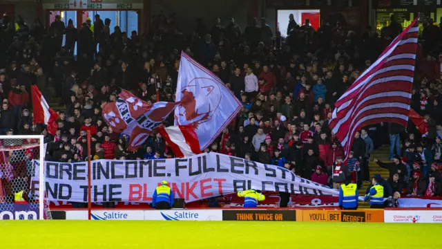 Aberdeen fans unveil a banner reading "More income. Fuller stands. End the blanket alcohol ban."