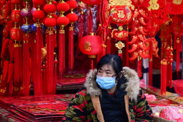 A vendor wearing a protective mask waits for customers at a stall selling Lunar New Year decorations at a market in Fuyang