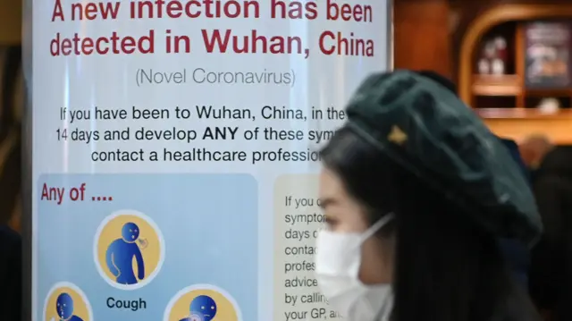 Woman wearing mask in front of warning sign