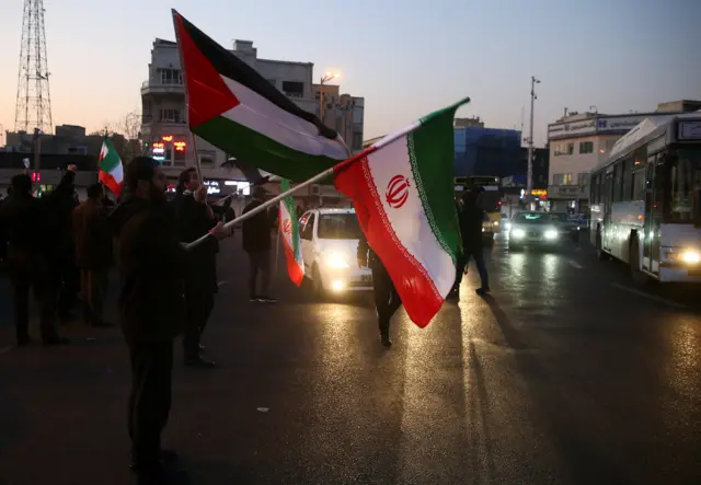 People in Tehran hold up Iranian and Palestinian flags as they celebrate the Iranian missile attack on US forces in Iraq