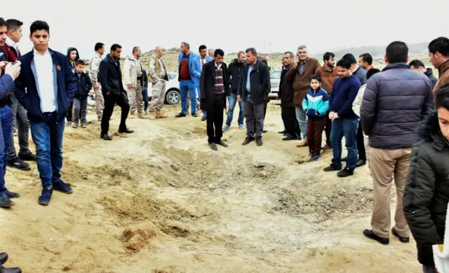 People stand beside a crater reportedly caused by an Iranian missile in Bardah Rashsh, in Iraq's Kurdistan Region