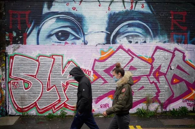 People wearing Covid-19 protective face masks walk past the remnants of a John Lennon mural on October 12, 2020 in Liverpool, England