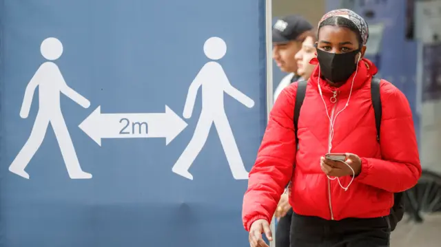 Person in mask alongside 2m sign