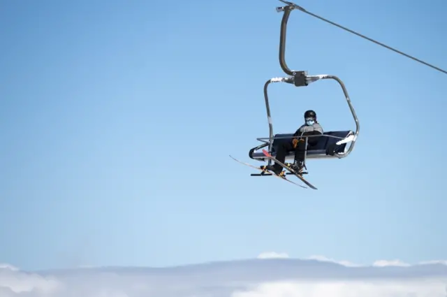 A person rides a ski lift while wearing a face mask